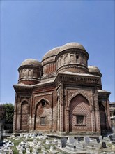 A brick mausoleum with multiple domes and arches under a clear sky