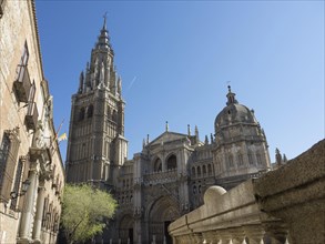 Historic cathedral with striking church tower, blue sky and stone wall in the foreground, toledo,