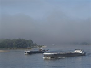 Two ships on a foggy river, trees and landscape in the background, ships on the rhine river in the