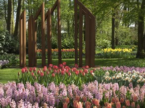 A colourful flower bed with tulips and hyacinths in a spring-like forest with a sculpture in the
