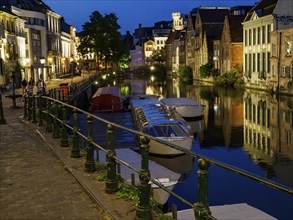 Night view of a canal with illuminated buildings, boats in the water and a railing in the