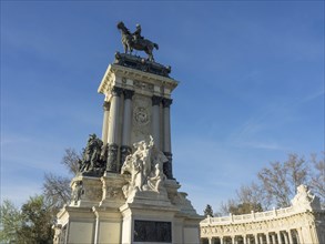 Tall equestrian statue on a horse, part of a large monument against a blue sky, Madrid, Spain,