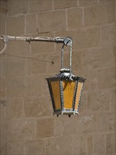Antique metal and glass lantern, suspended from a sturdy stone wall, gives a rustic ambience, the