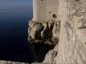 Stone fortress wall above rocky coastline on the calm sea, the old town of Dubrovnik with historic
