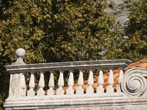 Close-up of a stone balcony balustrade with decorative ornaments and autumnal trees in the
