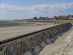 A beach with wooden constructions and houses in the background, sea and sky with some clouds,