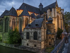 An old gothic church on a river, illuminated in warm evening light, blue hour in a medieval town