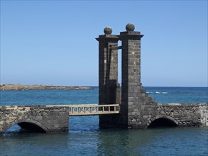 Two old stone towers with a small bridge over the water under a clear sky, the Canary Island of