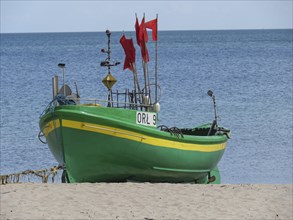 Green boat with red flags standing on sandy beach in front of calm sea under blue sky, green and
