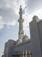 Detailed minaret and parts of a white mosque, shining under a sky with clouds, showing impressive