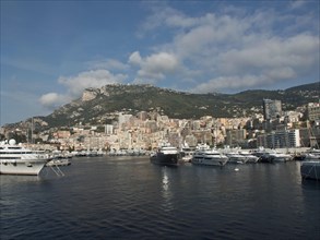 Harbour with several yachts in front of a city with mountains in the background under a slightly