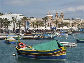 Boats in the harbour with a lively coastal town and palm trees in the background, colourful boats