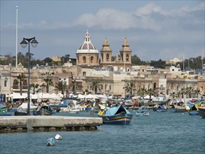 View of a seaside town with many fishing boats and historic buildings in the background, Valetta,