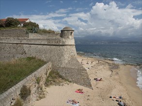Historic fortress on the beach with sand and blue sea under a slightly cloudy sky, Corsica,