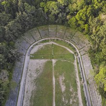 Aerial view of an ancient semicircular stadium with rows of stone seats surrounded by forest,