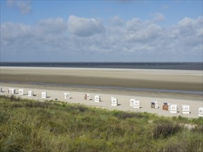 A wide beach with white beach chairs under a slightly cloudy sky. The sea stretches out in the