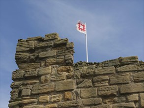 A stone castle ruin with a waving flag on a tower under a blue sky on a sunny day, old ruin by the