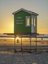 A green lifeguard hut on the beach while the sun sets in the background, evening mood on the beach