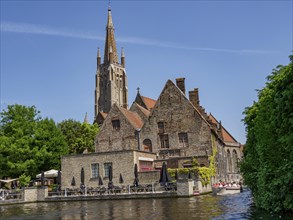 An old brick church building by the river with boats and green plants in summer, historic houses