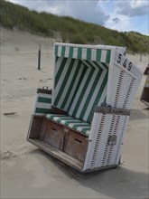 A single beach chair on the sandy beach in front of the dunes with grass under a cloudy sky, the