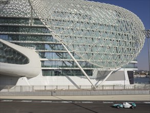 A racing car on a track next to a modern building with an impressive glass structure, dubai, arab