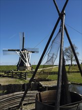 A traditional windmill next to fishing nets against a clear sky and green landscape, Enkhuizen,