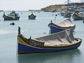 Fishing boats in the calm waters of a coastal town harbour under a clear sky, many colourful