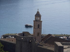 Historic church tower on the coast with a boat on the sea and a medieval city wall in the
