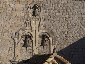 Historic bells on an old stone wall with a single bird on it in the afternoon sun, the old town of