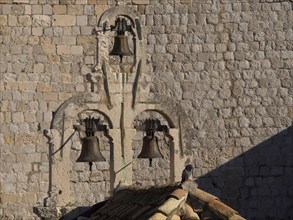 Historic bells on an old stone wall with a single bird on it in the afternoon sun, the old town of