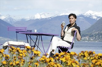 Woman Sitting in an Outdoor Restaurant and Drinking a Glass of Champagne with Snowcapped Mountain