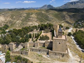 Aerial view of a historic fortress, surrounded by trees and mountains, with impressive walls and
