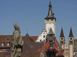 Historical statues in front of a clock tower with two church towers and lanterns with flowers, blue