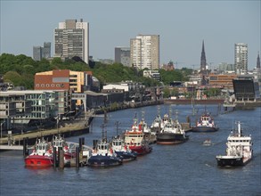 Several tugboats in Hamburg harbour, surrounded by urban buildings and clear skies, Gorse city on