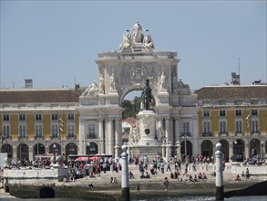 Impressive building with a large arch and sculptures in a lively city square, Lisbon, Portugal,