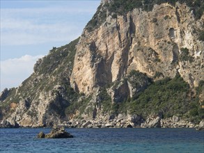 High cliffs by the sea, rocky landscape and deep blue water, beach on the island of Corfu with