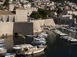 View of a harbour with numerous boats and historic stone walls, surrounded by buildings and