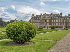 Well-kept symmetrical garden with hedges and paths in front of a historic castle under a cloudy