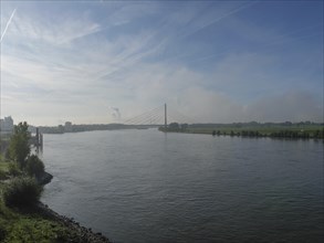 A wide river flows under a bridge, embedded in a quiet, natural landscape, ships on the rhine river