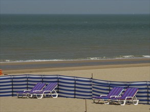 Wide view of a beach with blue and white striped deckchairs and a calm sea in the background,