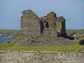 Stone ruins of an ancient building against a green landscape and blue sky, Green meadows by the sea