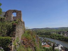 A historic ruin overlooks a picturesque green valley with a river under a sunny blue sky, castle