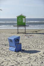 A green beach hut and a blue beach chair on a quiet beach in front of the sea and a clear sky,