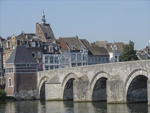 Historic stone bridge over the river with city and old buildings in the background, Maastricht,