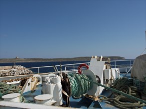 A fishing boat in the harbour with ropes and equipment, an island in the background under a clear