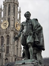Bronze statue in front of a historical tower with clocks under a cloudy sky, Historical buildings