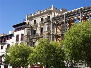 Multi-storey historic building with balcony facades and green trees below, palma de Majorca with