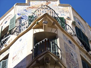 A building with decorative mosaics and balconies, green shutters and an ornate facade, palma de