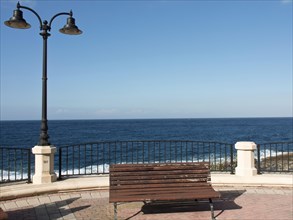 A wooden bench in front of a metal railing with sea and sky in the background, Valetta, Malta,