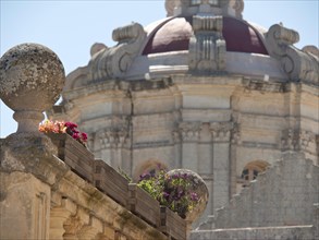 Detail view of a historical architecture with a dome in the background and flowers on a stone wall,